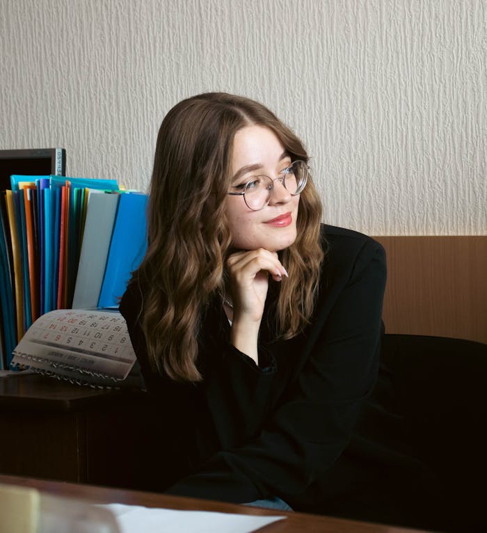 Portrait of a young woman in an office environment, looking thoughtful with a calendar and colored folders.
