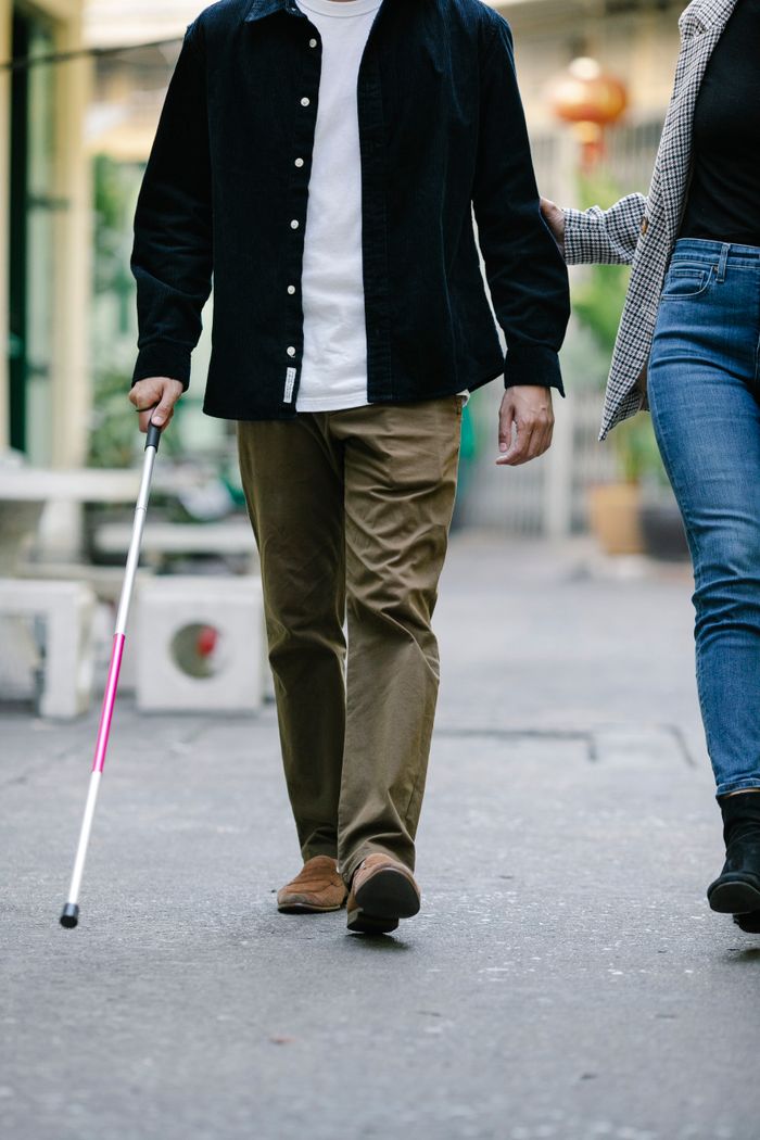 A visually impaired man with a cane and a woman walking outdoors, emphasizing assistance and guidance.